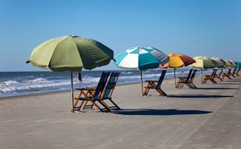 Sun chairs and sun umbrellas on a sandy beach against a clear blue sky in Galveston, Texas